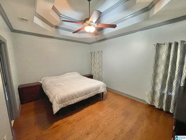 bedroom with a tray ceiling, hardwood / wood-style floors, ceiling fan, and crown molding