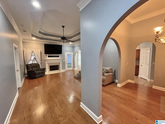 unfurnished living room featuring hardwood / wood-style flooring, ceiling fan, a raised ceiling, and crown molding