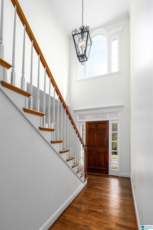 entryway featuring dark wood-type flooring, a high ceiling, a notable chandelier, and ornamental molding