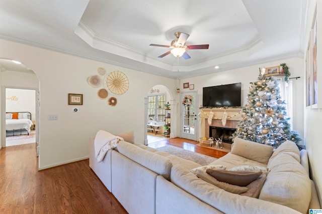 living room with ceiling fan, crown molding, a raised ceiling, and dark hardwood / wood-style flooring