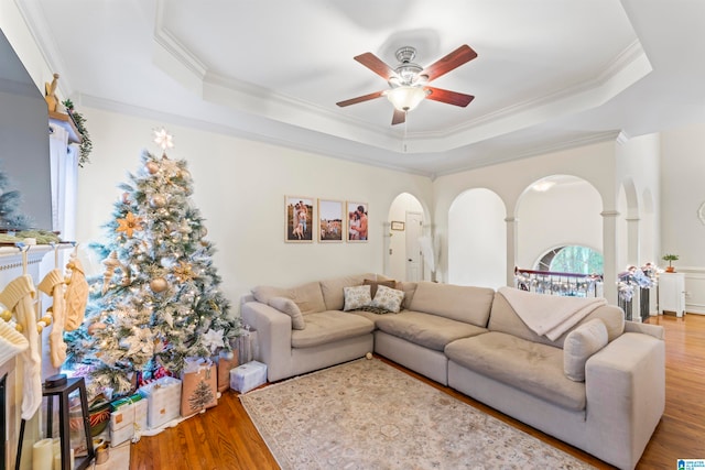 living room with ceiling fan, wood-type flooring, a raised ceiling, and ornamental molding