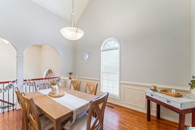 dining area with wood-type flooring, high vaulted ceiling, and ornamental molding