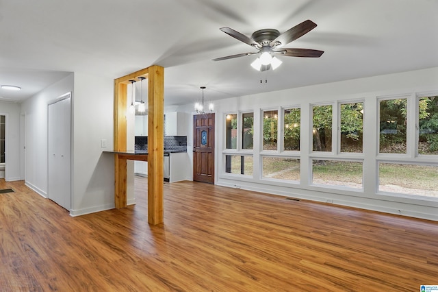 unfurnished living room featuring ceiling fan with notable chandelier and light wood-type flooring