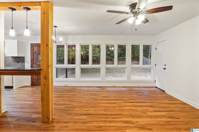 unfurnished living room with light wood-type flooring and ceiling fan with notable chandelier