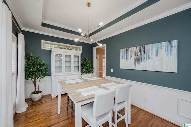 dining area featuring hardwood / wood-style floors, a notable chandelier, a tray ceiling, and ornamental molding