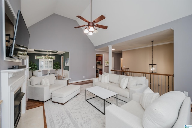 living room featuring ornate columns, ceiling fan with notable chandelier, high vaulted ceiling, crown molding, and light hardwood / wood-style flooring