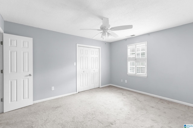 unfurnished bedroom with a textured ceiling, light colored carpet, ceiling fan, and a closet