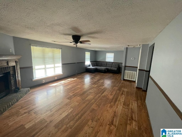 unfurnished living room featuring ceiling fan, dark hardwood / wood-style flooring, a textured ceiling, and a brick fireplace