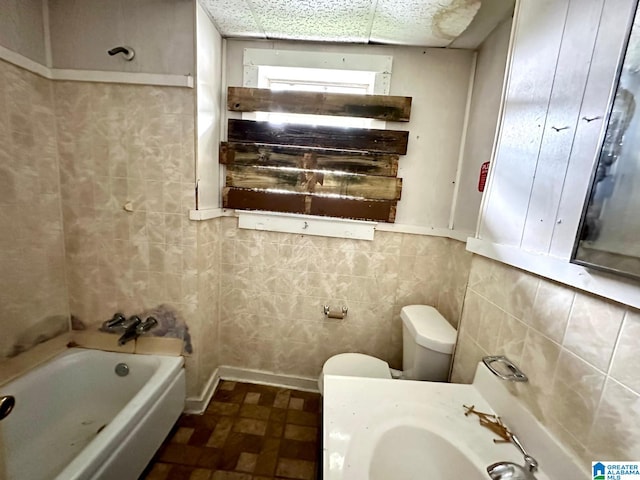 bathroom featuring tile walls, a tub to relax in, and toilet