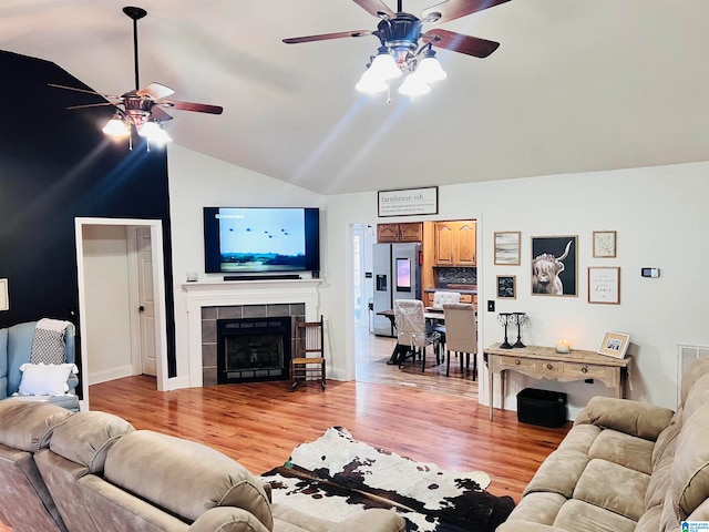 living room featuring ceiling fan, lofted ceiling, light hardwood / wood-style floors, and a fireplace