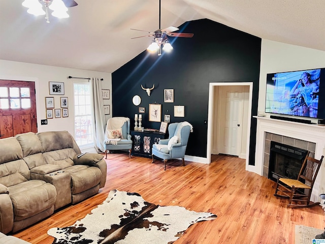 living room featuring ceiling fan, a tile fireplace, light wood-type flooring, and vaulted ceiling