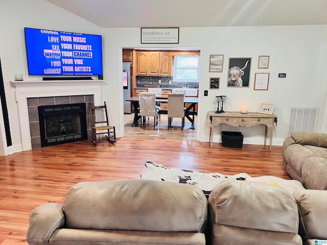 living room featuring a fireplace, vaulted ceiling, and light hardwood / wood-style flooring