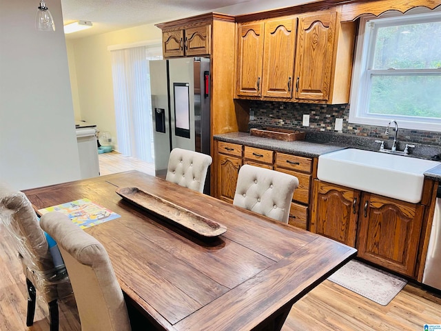 kitchen featuring decorative backsplash, sink, light wood-type flooring, and stainless steel fridge with ice dispenser