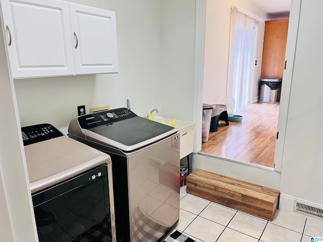 clothes washing area with light hardwood / wood-style floors, cabinets, sink, and washer and dryer