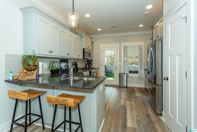 kitchen with tasteful backsplash, appliances with stainless steel finishes, hanging light fixtures, dark wood-type flooring, and kitchen peninsula