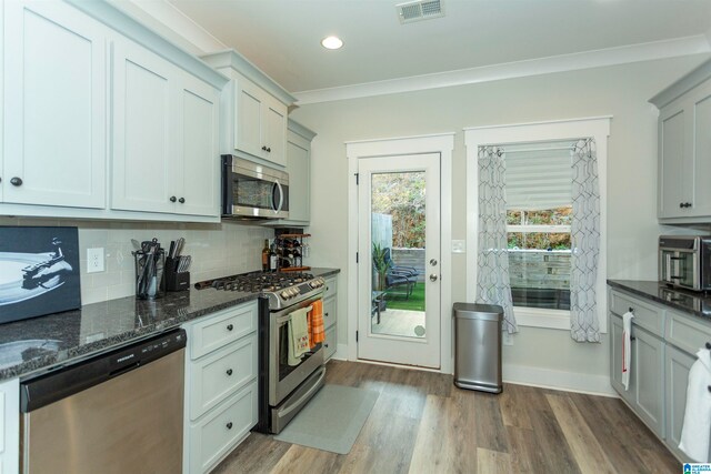 kitchen featuring stainless steel appliances, dark hardwood / wood-style floors, dark stone countertops, backsplash, and crown molding