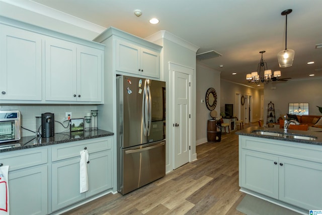 kitchen featuring sink, tasteful backsplash, light wood-type flooring, decorative light fixtures, and stainless steel fridge