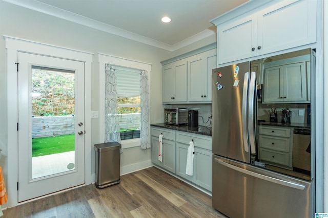 kitchen with dark hardwood / wood-style flooring, dark stone counters, decorative backsplash, crown molding, and appliances with stainless steel finishes