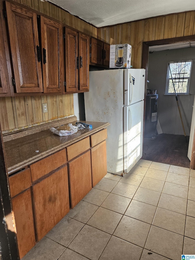 kitchen with light tile patterned flooring, wood walls, white fridge, and a textured ceiling