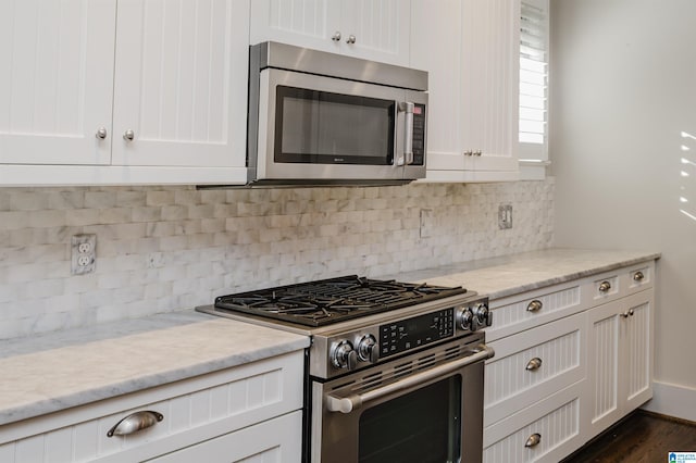 kitchen with stainless steel appliances, light stone countertops, white cabinetry, and tasteful backsplash