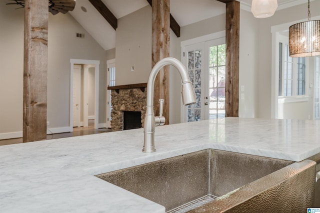 kitchen with sink, beam ceiling, hanging light fixtures, a stone fireplace, and french doors