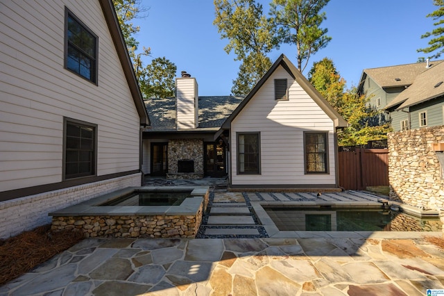 rear view of property with a patio area and an in ground hot tub