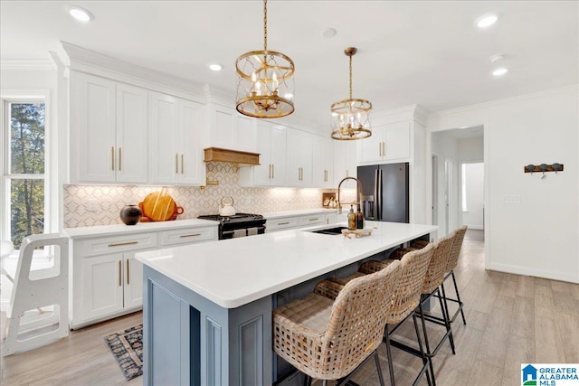 kitchen featuring stainless steel appliances, a center island with sink, white cabinetry, light wood-type flooring, and pendant lighting