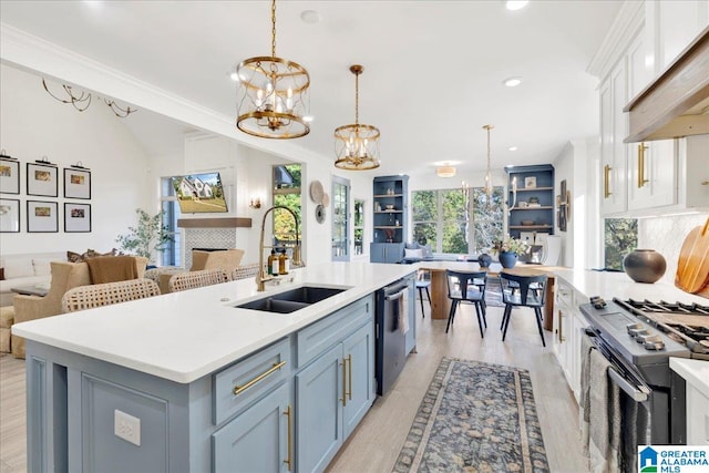 kitchen featuring white cabinetry, sink, appliances with stainless steel finishes, decorative light fixtures, and an island with sink