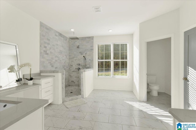 bathroom with tiled shower, vanity, and toilet