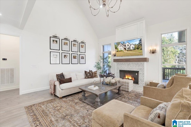 living room featuring a tiled fireplace, light hardwood / wood-style floors, an inviting chandelier, high vaulted ceiling, and beamed ceiling