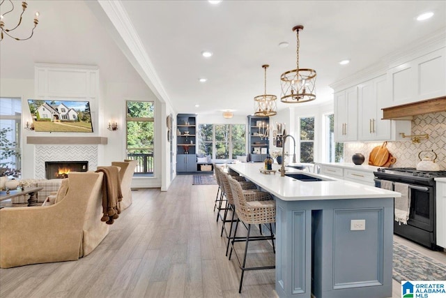 kitchen with a center island with sink, light hardwood / wood-style flooring, white cabinetry, and stainless steel range oven