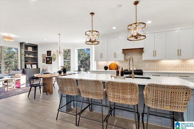 kitchen with light hardwood / wood-style flooring, decorative light fixtures, a center island with sink, and white cabinets