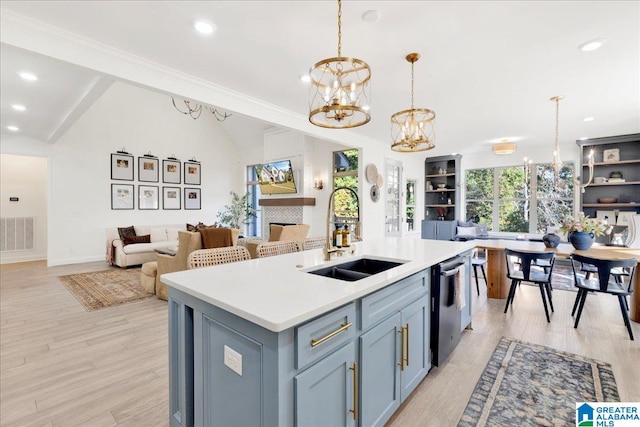 kitchen with a center island with sink, sink, hanging light fixtures, light wood-type flooring, and dishwasher