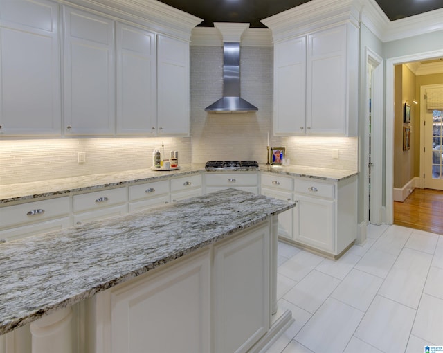 kitchen featuring white cabinetry, backsplash, stainless steel gas stovetop, crown molding, and wall chimney range hood