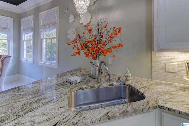 details featuring sink, light stone counters, ornamental molding, white cabinets, and decorative backsplash