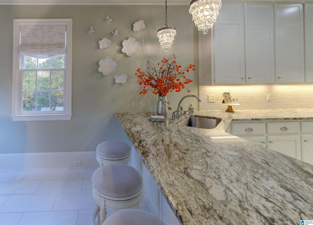 kitchen featuring light stone counters, backsplash, decorative light fixtures, sink, and white cabinets