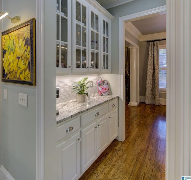 bar featuring light stone counters, crown molding, ornate columns, white cabinets, and dark wood-type flooring