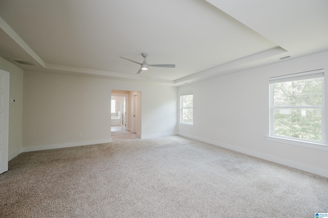 spare room with ceiling fan, light carpet, and a raised ceiling