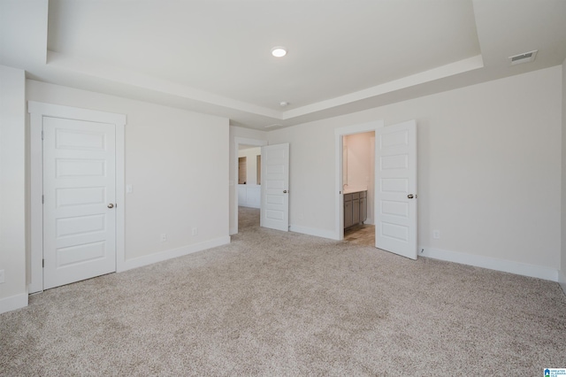 unfurnished bedroom featuring ensuite bath, light carpet, a tray ceiling, and a closet