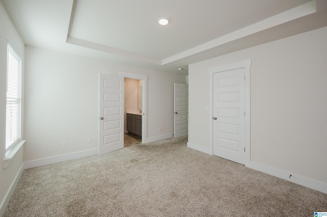 unfurnished bedroom featuring a closet, light colored carpet, a raised ceiling, and connected bathroom