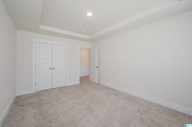 unfurnished bedroom featuring carpet flooring, a closet, and a tray ceiling