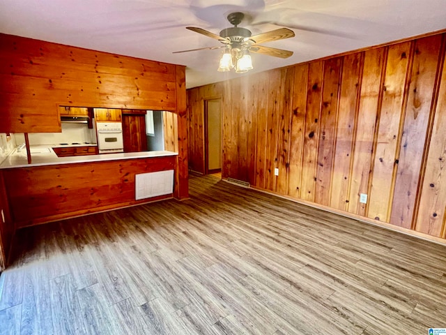 kitchen featuring kitchen peninsula, wooden walls, hardwood / wood-style floors, and white oven