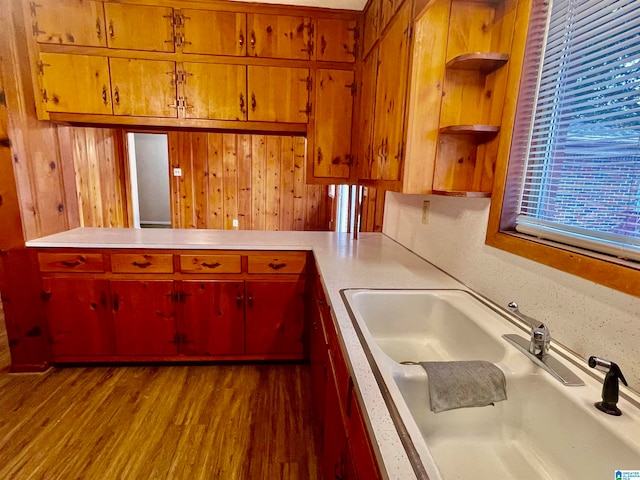 kitchen with wood walls, kitchen peninsula, hardwood / wood-style floors, and sink