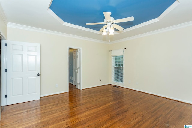 empty room with dark wood-type flooring, a raised ceiling, ceiling fan, and crown molding