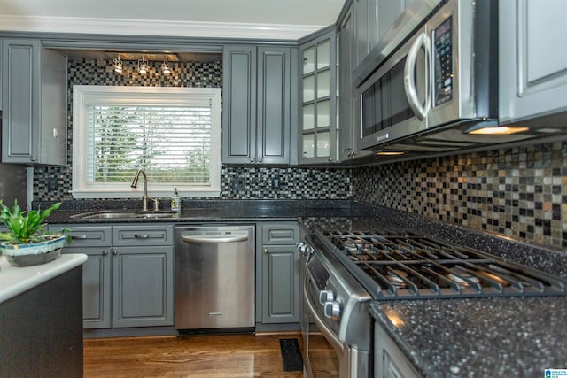 kitchen featuring stainless steel appliances, sink, dark stone counters, backsplash, and wood-type flooring