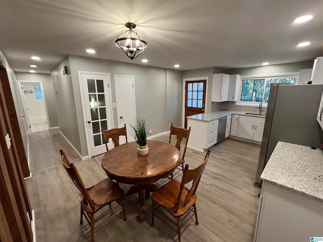 dining space with an inviting chandelier, sink, and light hardwood / wood-style flooring