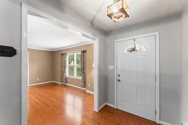 foyer entrance with wood-type flooring, crown molding, and a textured ceiling