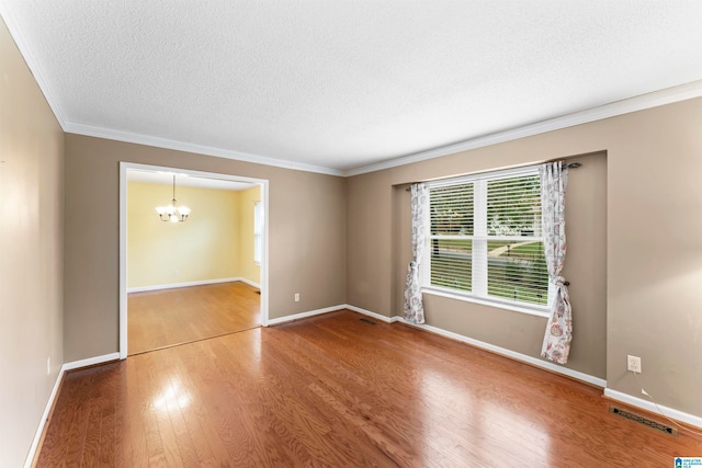 spare room with hardwood / wood-style floors, a textured ceiling, ornamental molding, and a notable chandelier