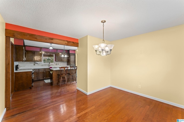 unfurnished dining area featuring a textured ceiling, an inviting chandelier, and dark wood-type flooring