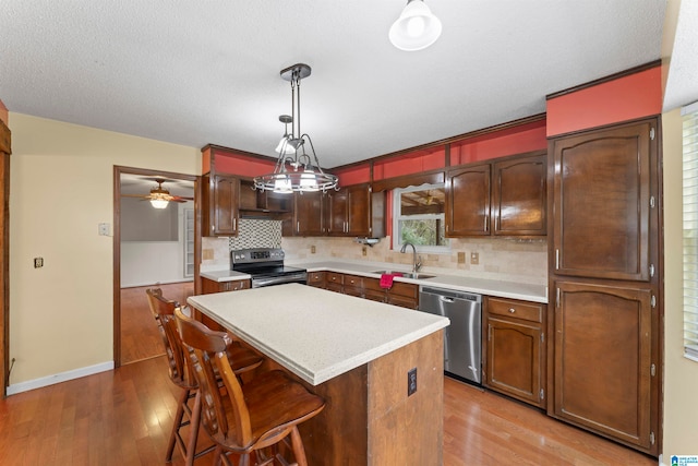 kitchen with appliances with stainless steel finishes, tasteful backsplash, pendant lighting, a center island, and light hardwood / wood-style floors